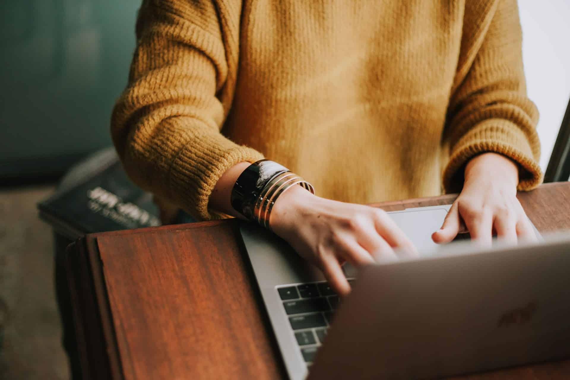 Eine Person sitzt vor einem Laptop, man sieht einen Teil des Laptops und des Oberkörpers, aber nicht das Gesicht